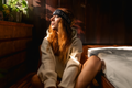 Woman wearing the audicin headband sitting beside a bed in a dimly lit room.